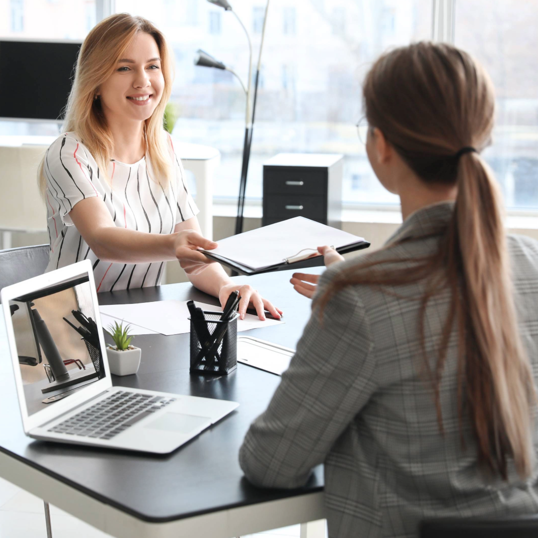 a women handing over a file to another women in a office setting 