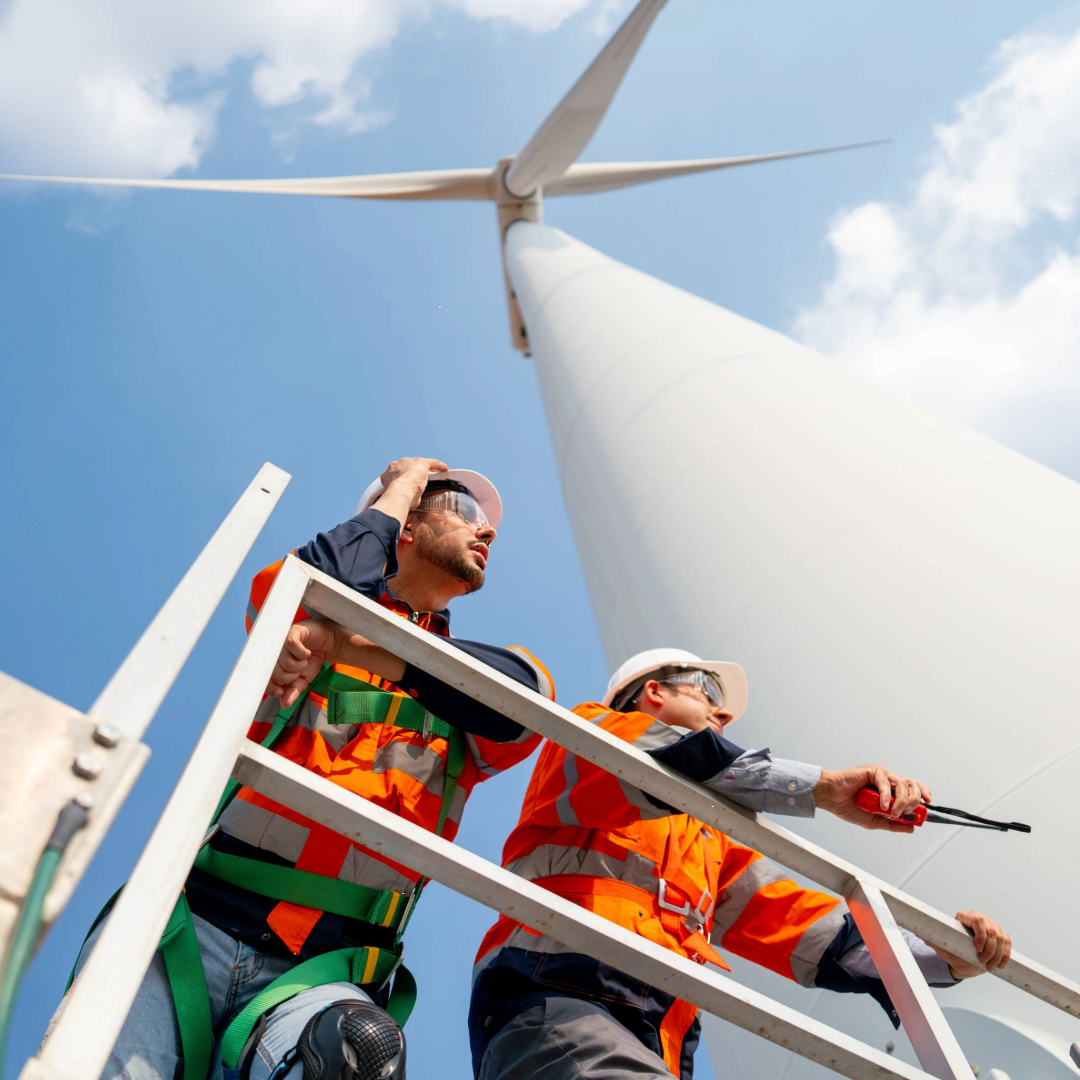 two workers standing under a wind turbine