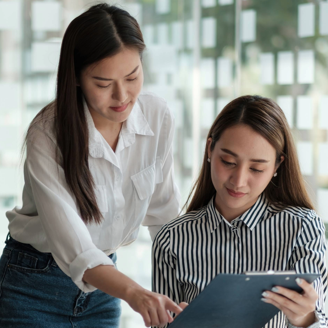 two women looking at work on a clip board 