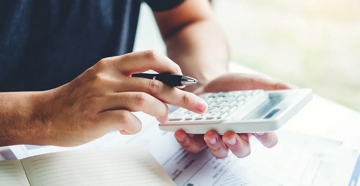 Man holding pen in right hand while holding calculator with left hand