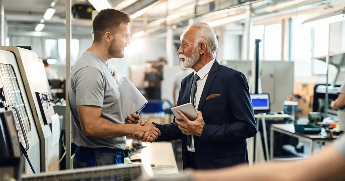 Two men standing up while shaking hands in factory