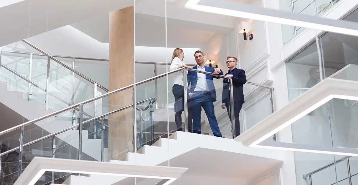 Three people talking to one another at the top of a glass staircase