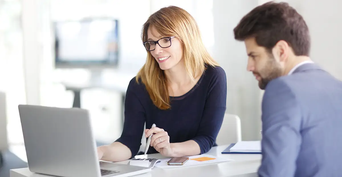 Woman with glasses using laptop while man looks over