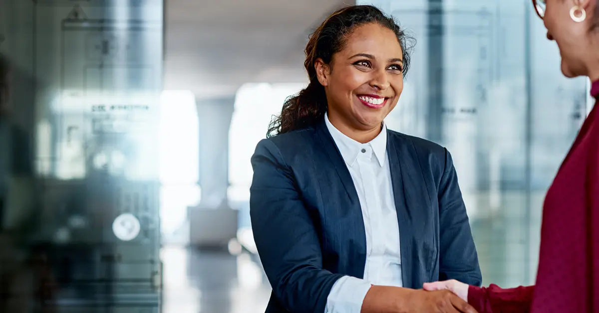 Woman smiling while shaking someones hand in an office environment