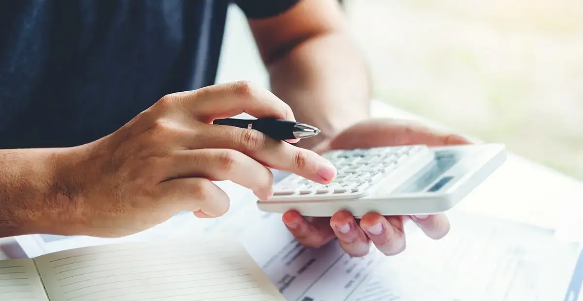 Man holding pen in right hand while using calculator