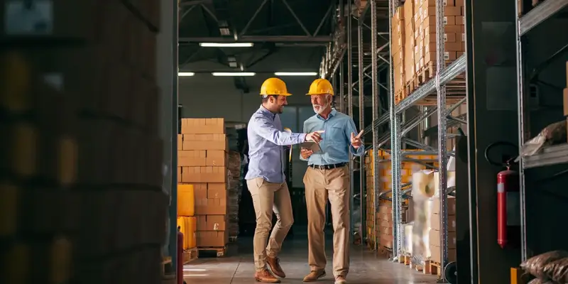 Two men with yellow safety helmets inside a warehouse