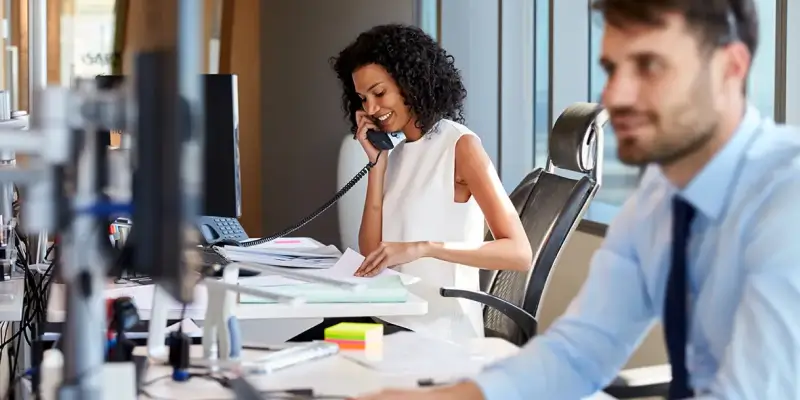 Woman smiling while holding telephone up to right ear in an office