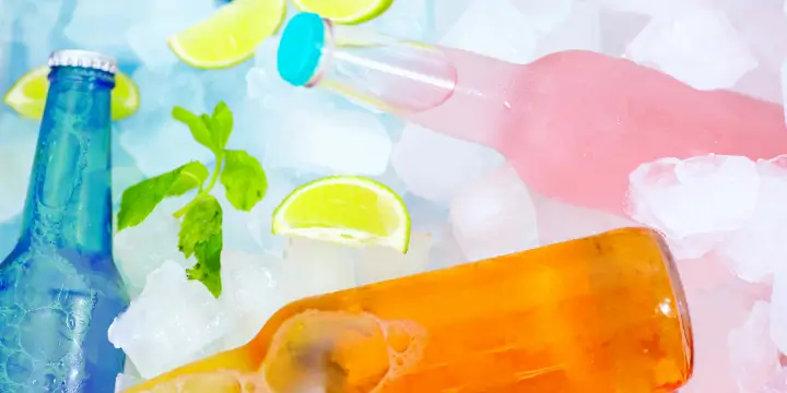 Three glass soft drink bottles sitting in ice cubes with slices of lime