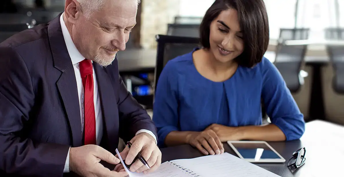 Man and woman looking at notepad while sitting at desk