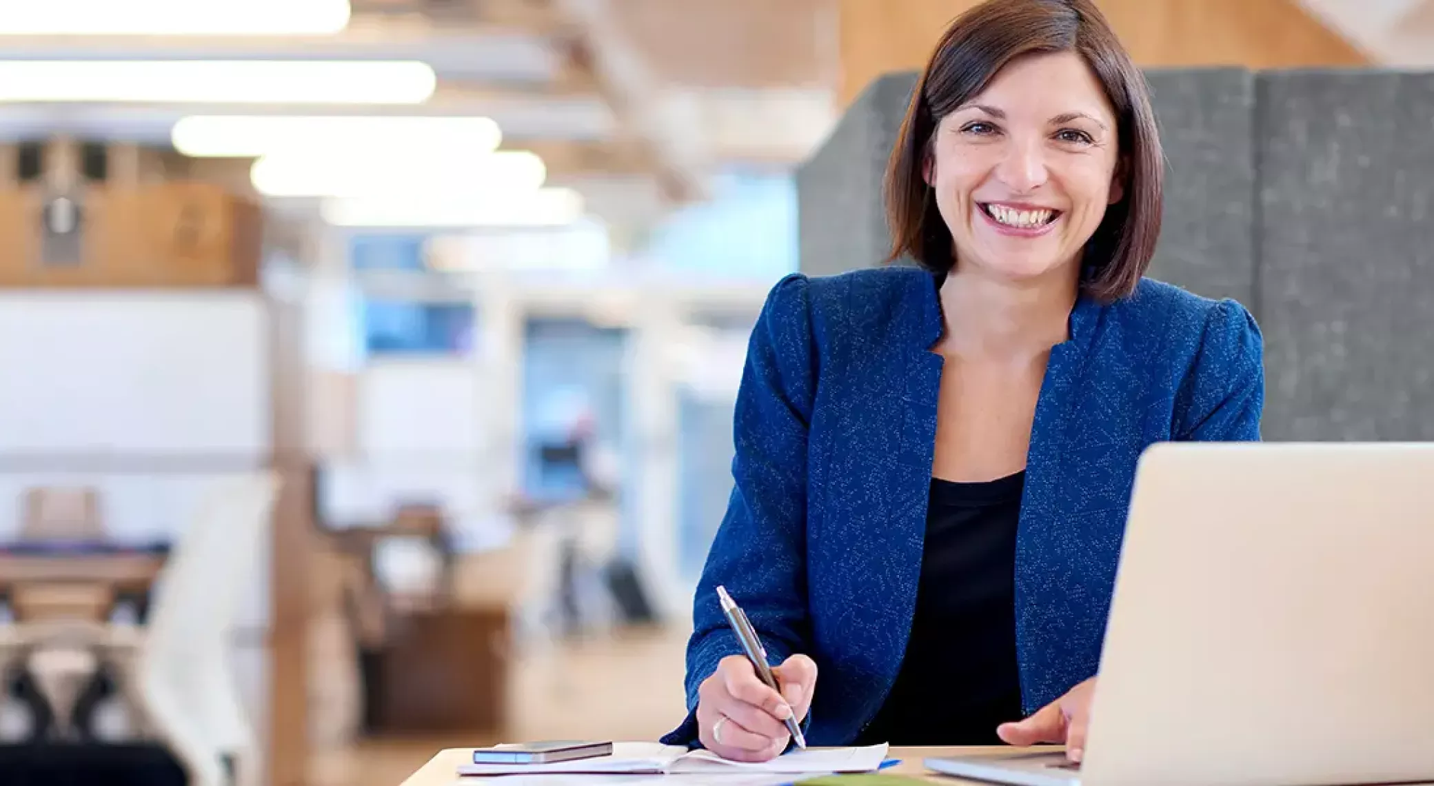 Woman sat down smiling while looking at camera and writing with right hand