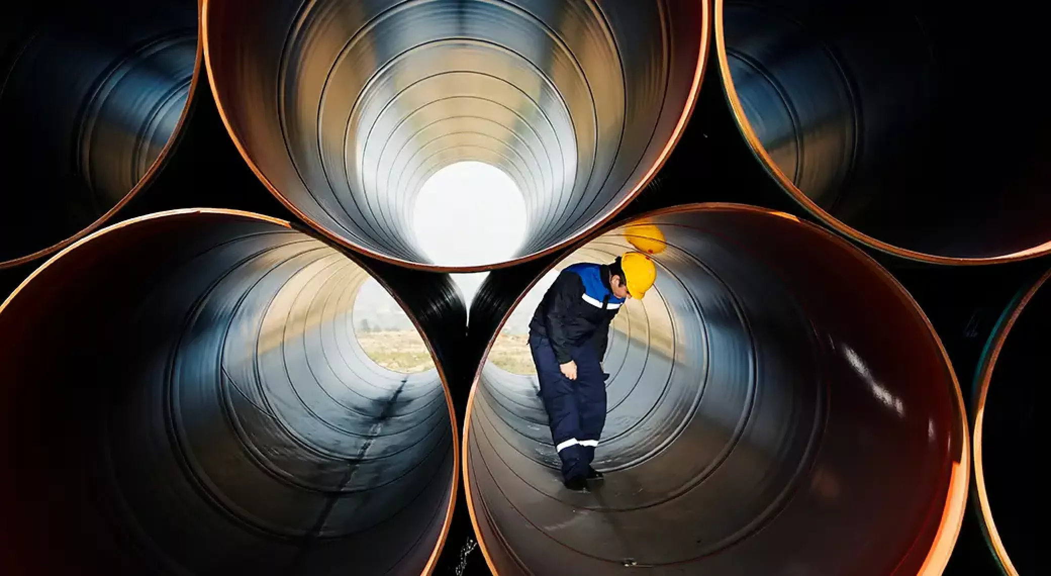 Man with yellow hard hat looking down while inside of large water pipe