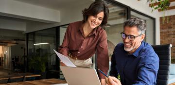 two people looking at a laptop with a paper in hand